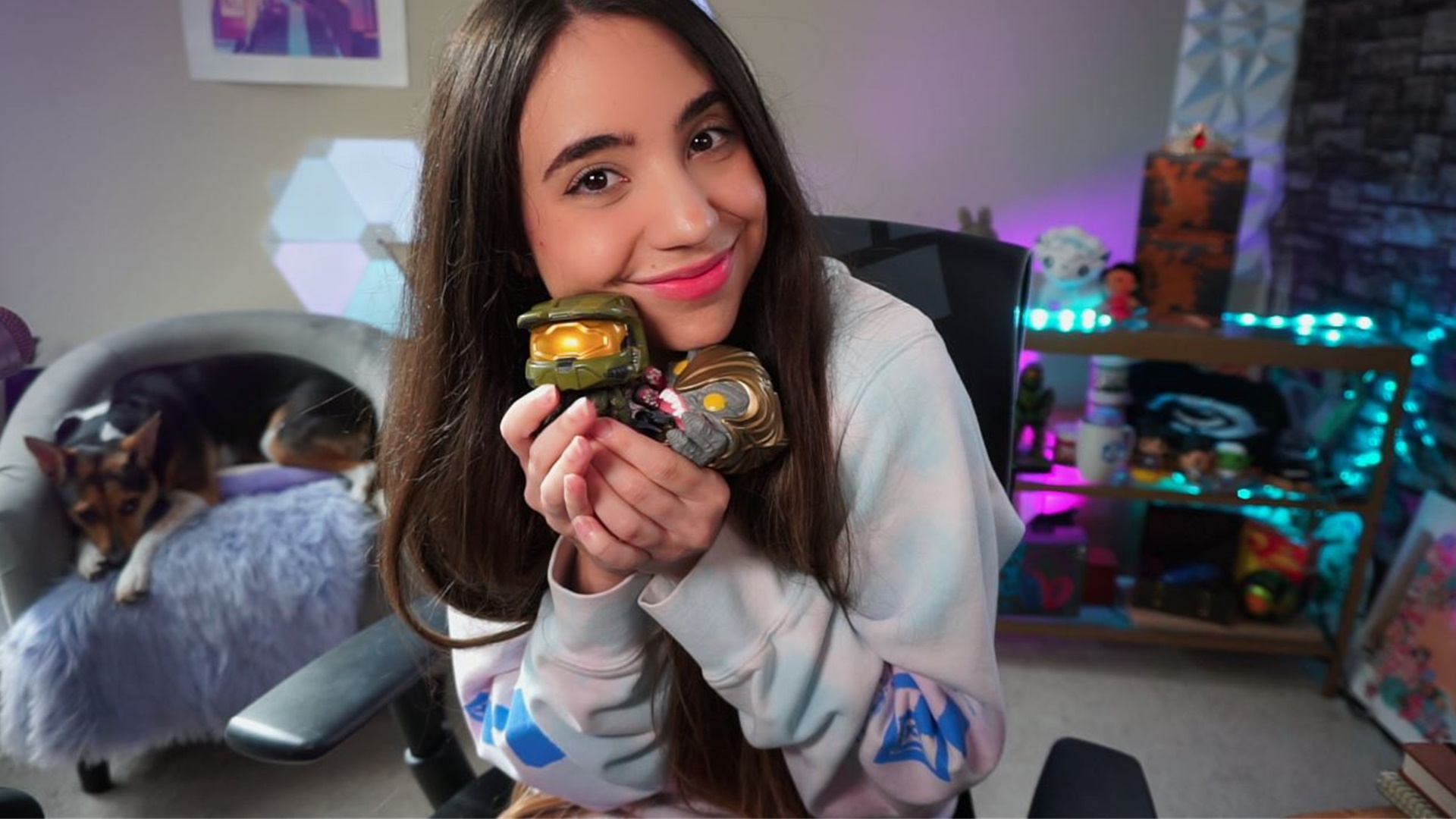 Photograph of Alyek in her room holding Funko figures of the Master Chief and the Arbiter
