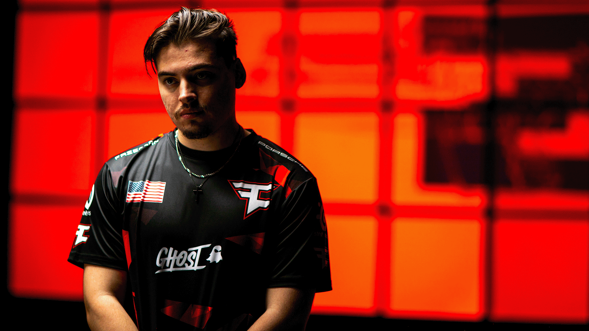 Renegade, from Faze Clan, poses in front of a red screen while wearing a Faze Clan jersey.