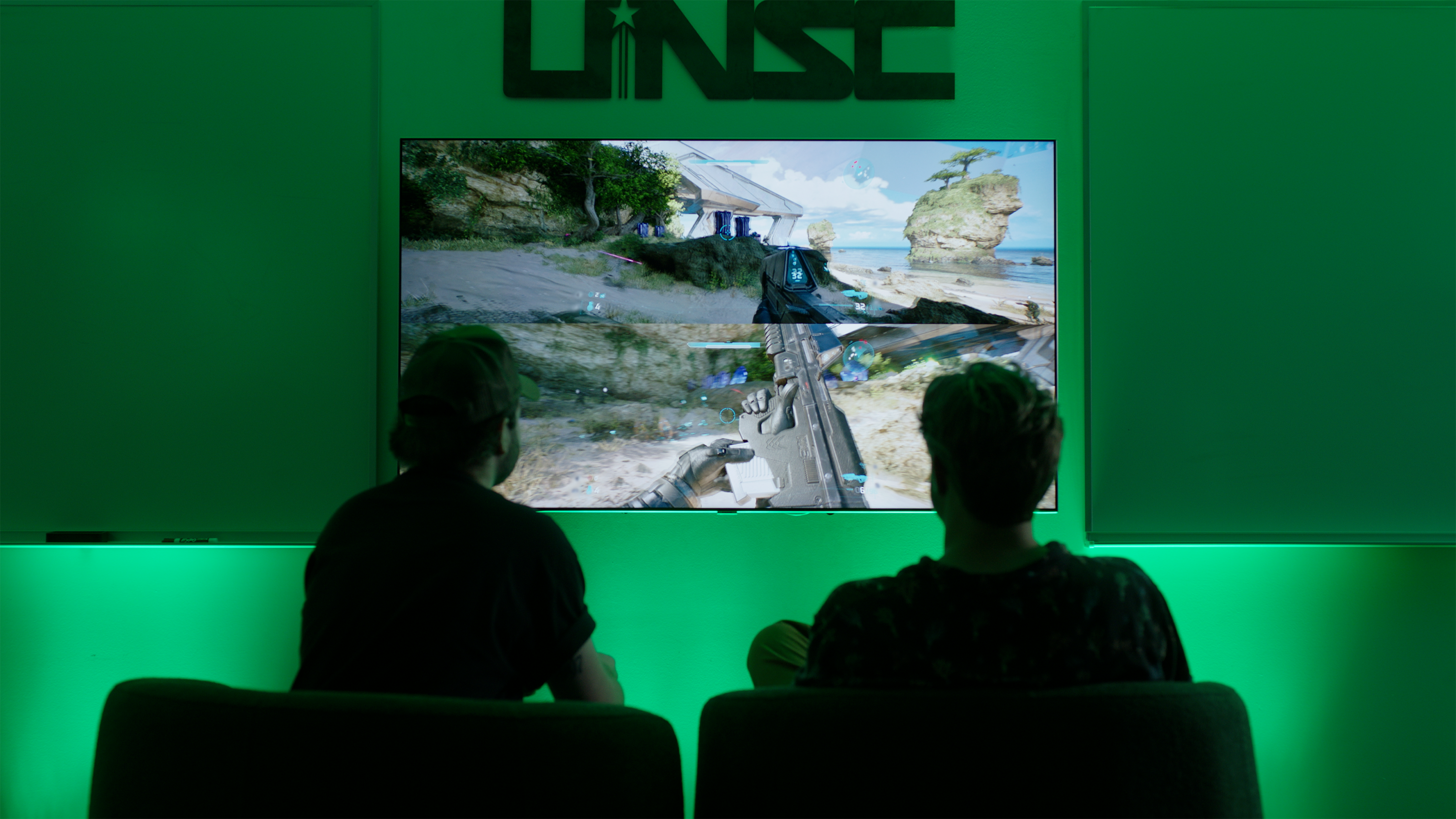 Two gamers sit in armchairs playing split-screen co-op in Halo: Campaign Evolved.
