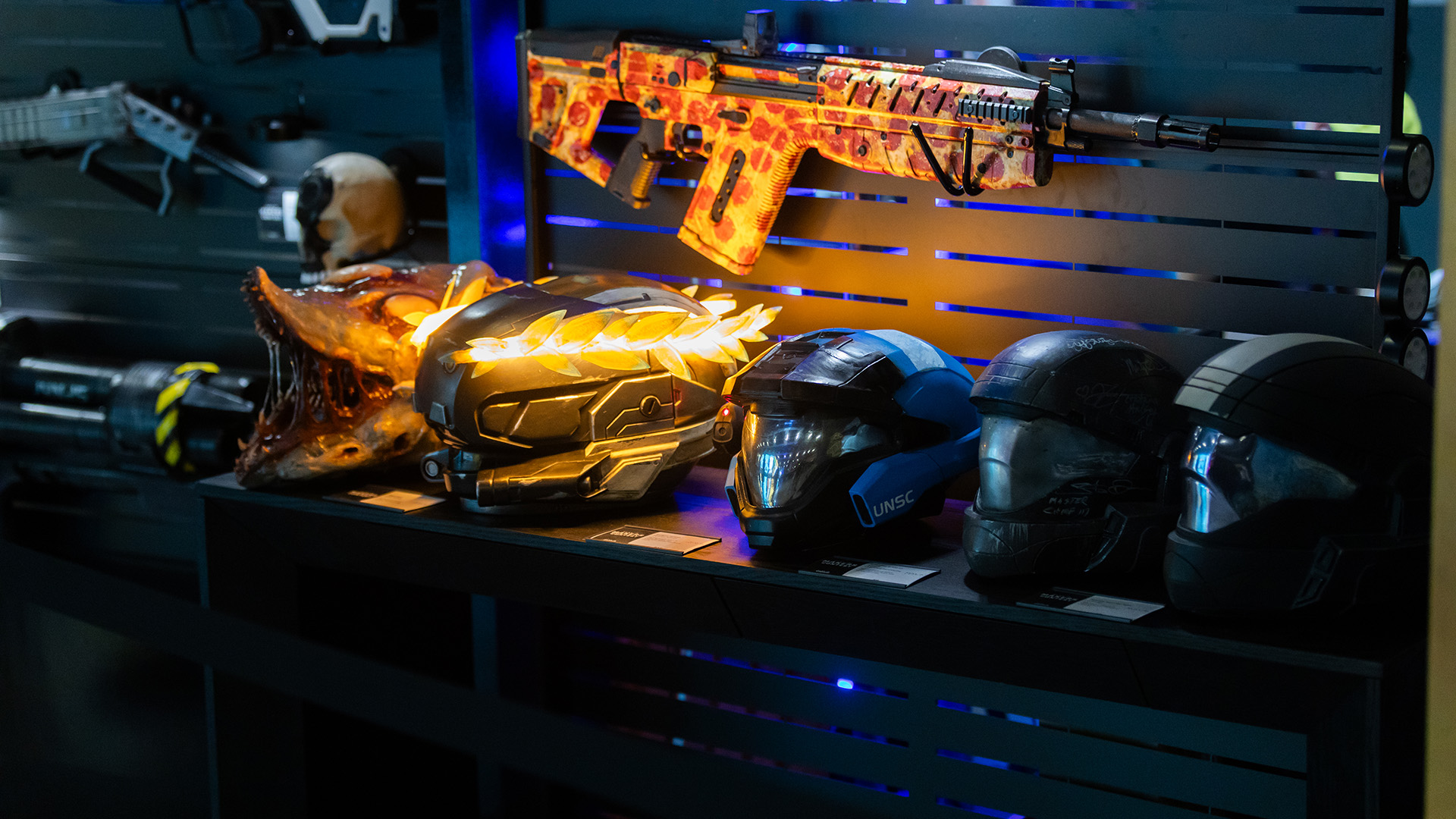 A row of custom Spartan helmets sits under a VK78 Commando replica painted with a pepperoni pizza design.