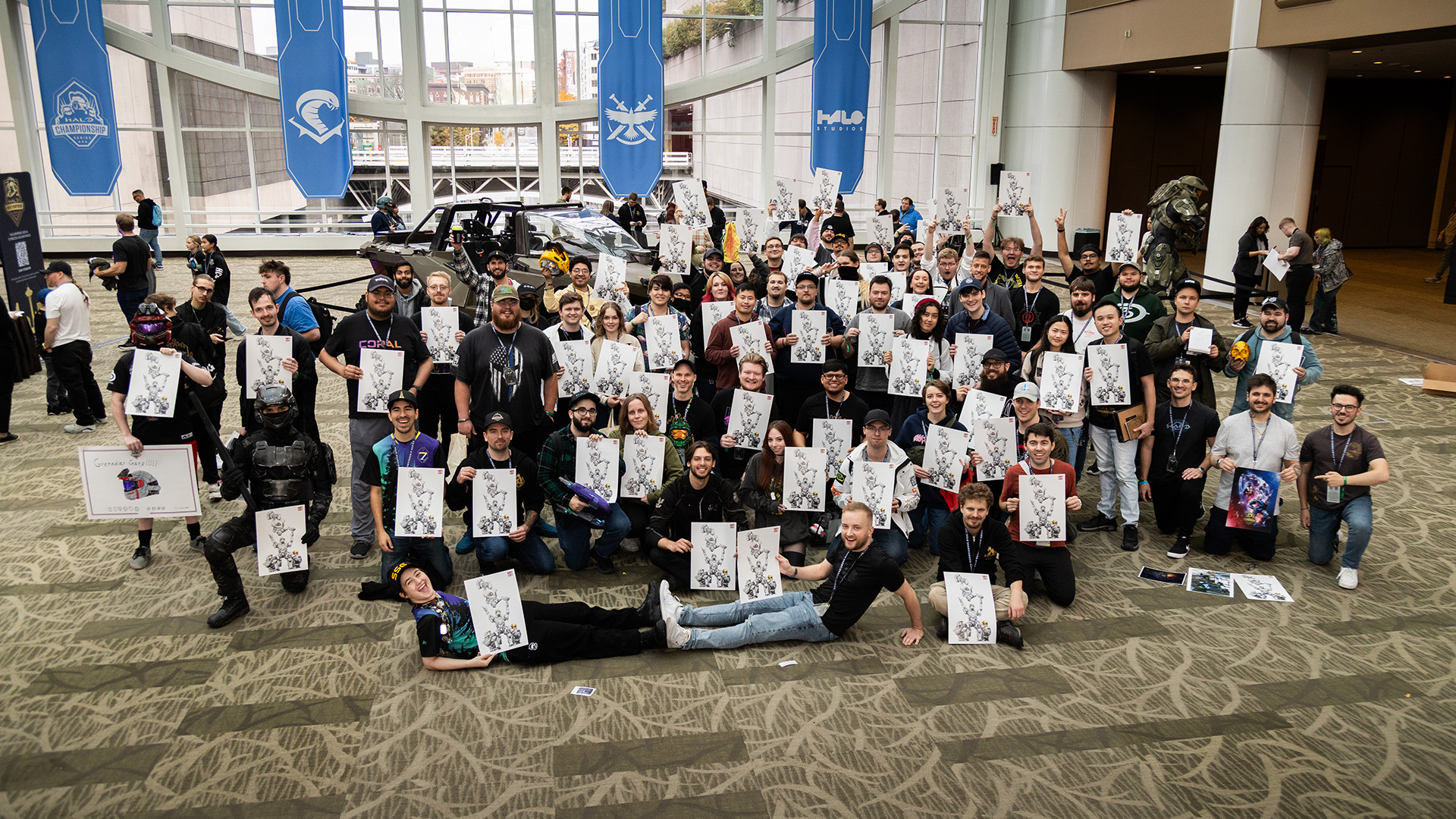 A group photo of Halo fans and members of the Halo Studios Community Team holding entransing's poster design at a community meet-up.